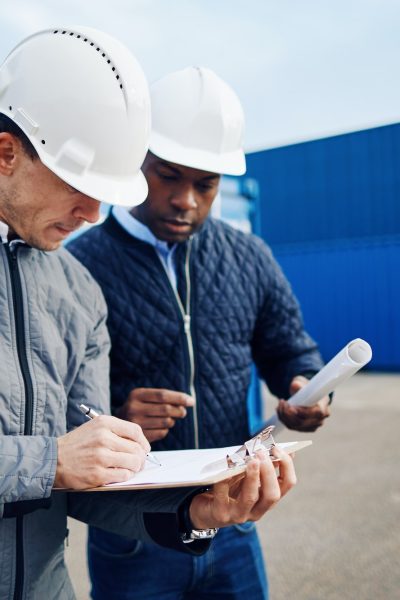 Two engineers standing in a shipping yard discussing logistics